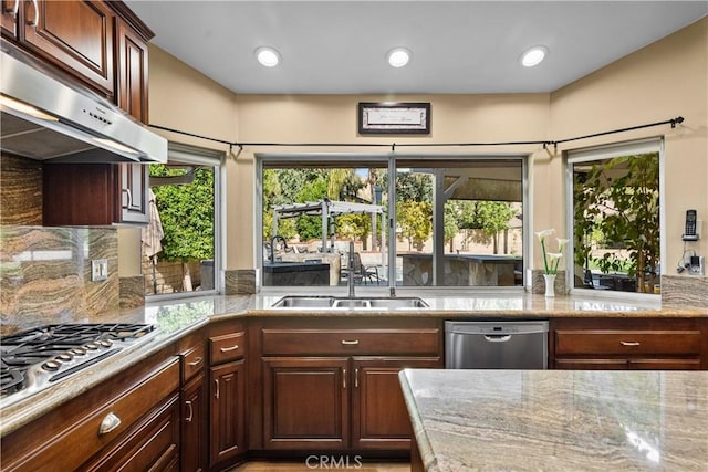 kitchen with backsplash, appliances with stainless steel finishes, a sink, light stone countertops, and under cabinet range hood