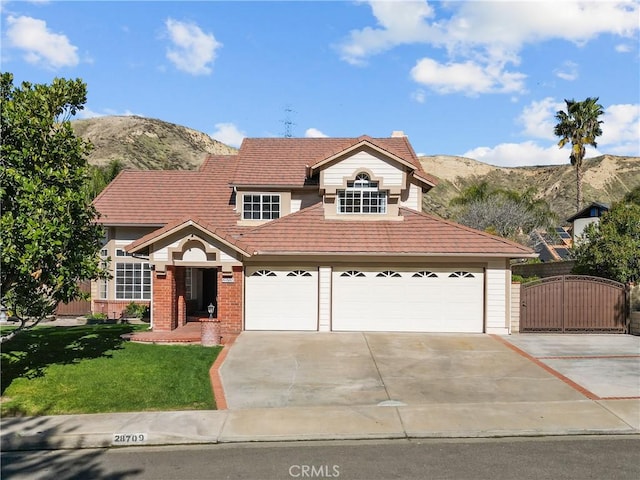 traditional-style house with concrete driveway, an attached garage, a gate, a mountain view, and brick siding