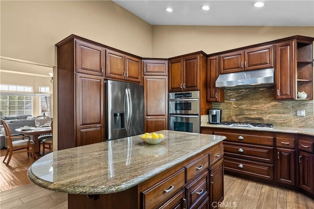 kitchen with light stone countertops, under cabinet range hood, stainless steel appliances, light wood-style floors, and a center island