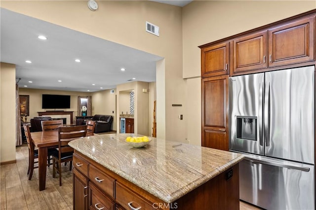 kitchen featuring light stone countertops, a center island, visible vents, and stainless steel fridge with ice dispenser