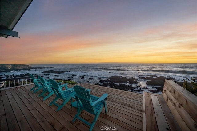 deck at dusk featuring a water view and a beach view