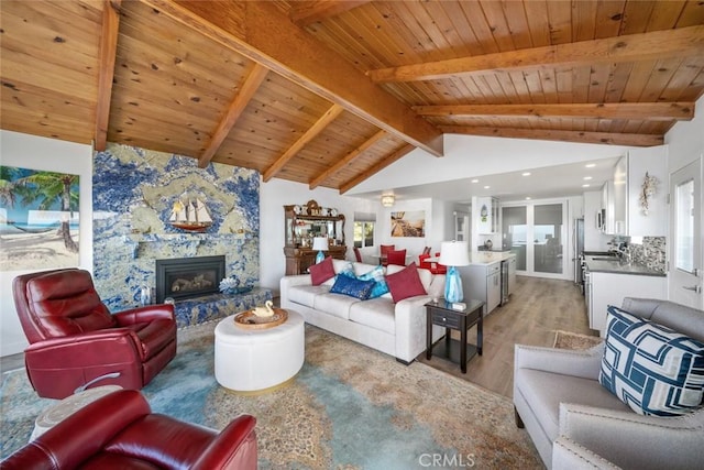 living area featuring lofted ceiling with beams, wood ceiling, wood finished floors, and a stone fireplace