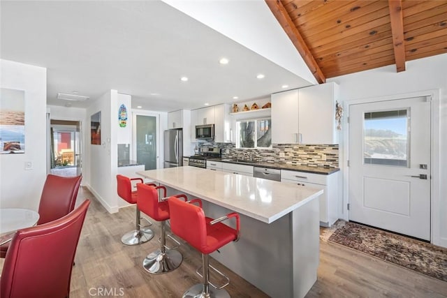 kitchen with a center island, tasteful backsplash, lofted ceiling with beams, appliances with stainless steel finishes, and white cabinetry