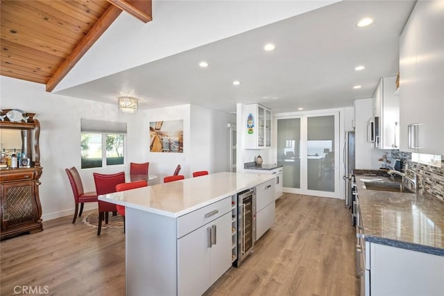 kitchen with lofted ceiling with beams, wine cooler, a center island, and white cabinets
