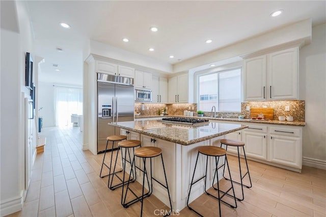 kitchen featuring light stone counters, a center island, white cabinetry, and built in appliances