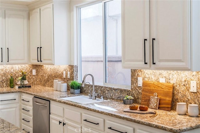 kitchen with a healthy amount of sunlight, light stone countertops, white cabinets, and a sink