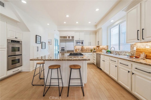 kitchen with built in appliances, light stone counters, a kitchen island, white cabinets, and backsplash