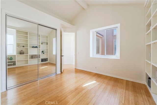 unfurnished bedroom featuring lofted ceiling with beams, hardwood / wood-style floors, a closet, and baseboards