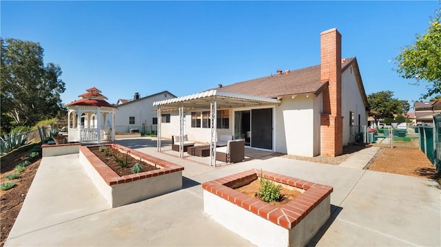 back of house with a patio, a chimney, fence, a gazebo, and stucco siding