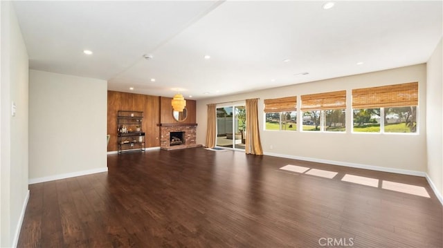 unfurnished living room featuring baseboards, a fireplace with raised hearth, dark wood finished floors, and recessed lighting