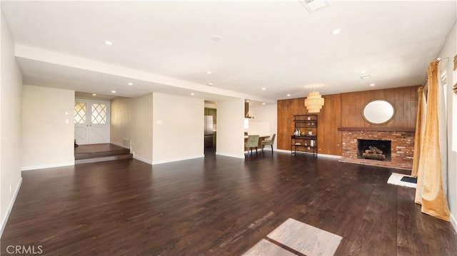 unfurnished living room featuring a brick fireplace, baseboards, dark wood-type flooring, and recessed lighting