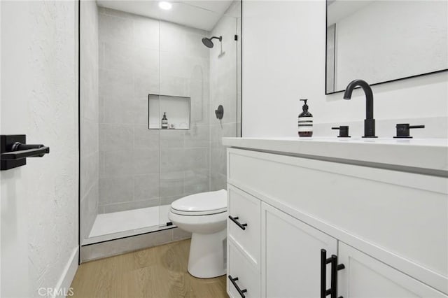 bathroom featuring a textured wall, toilet, wood finished floors, vanity, and a stall shower