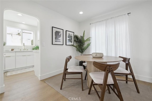 dining area featuring light wood-style flooring, baseboards, arched walkways, and recessed lighting