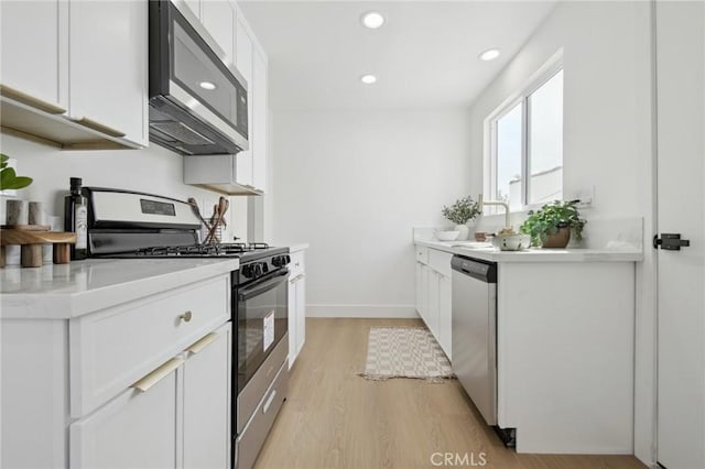 kitchen with recessed lighting, light countertops, light wood-style flooring, appliances with stainless steel finishes, and white cabinetry