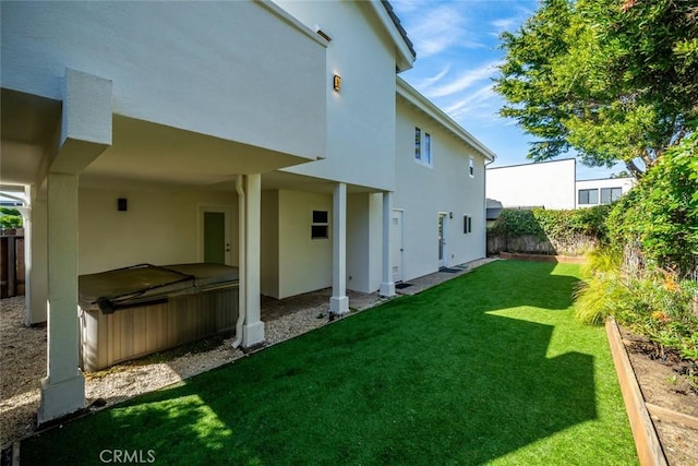 rear view of house with a fenced backyard, a lawn, a hot tub, and stucco siding