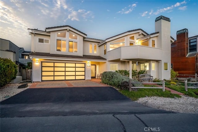 view of front of home featuring driveway, a garage, a balcony, a chimney, and stucco siding