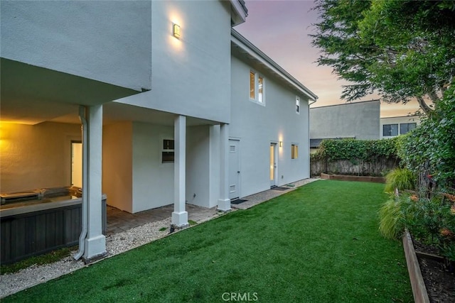 back of house at dusk with a lawn, fence, and stucco siding