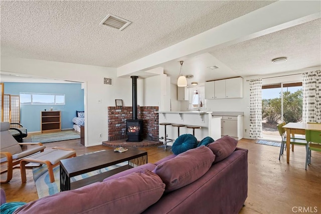 living area featuring a wood stove, visible vents, a textured ceiling, and baseboards