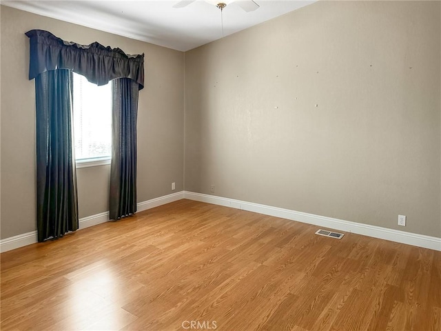 empty room featuring wood finished floors, visible vents, and baseboards