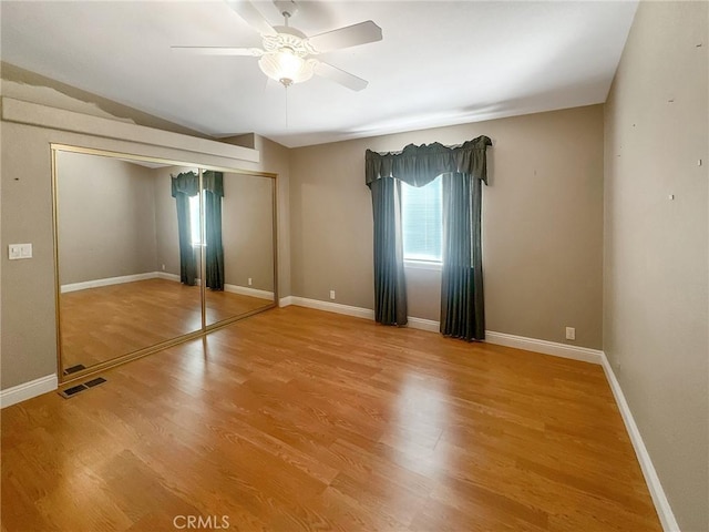 unfurnished bedroom with a closet, visible vents, ceiling fan, wood finished floors, and baseboards