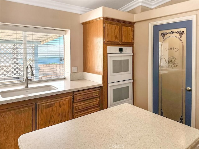 kitchen featuring ornamental molding, brown cabinets, light countertops, double oven, and a sink