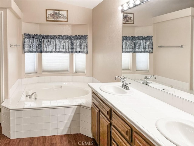 full bathroom featuring double vanity, a garden tub, a sink, and wood finished floors