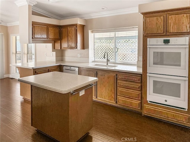 kitchen with white appliances, a sink, light countertops, ornamental molding, and a center island