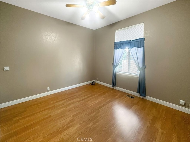 spare room with a ceiling fan, visible vents, baseboards, and wood finished floors