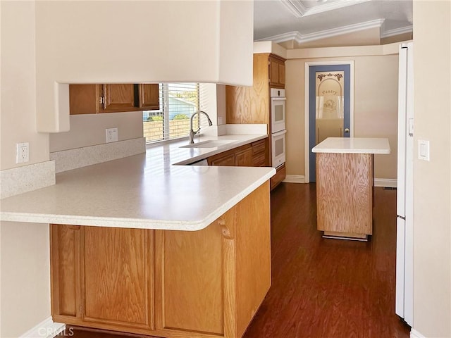 kitchen with dark wood-style flooring, brown cabinets, light countertops, a sink, and a peninsula