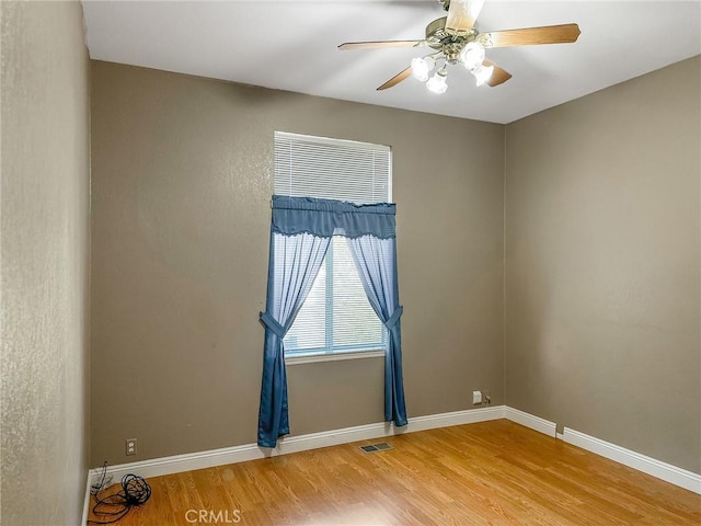 unfurnished room featuring a ceiling fan, baseboards, visible vents, and wood finished floors