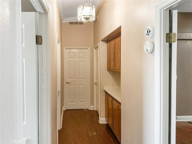 corridor featuring visible vents, baseboards, ornamental molding, dark wood-style floors, and an inviting chandelier