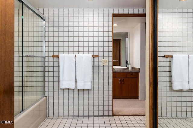 bathroom with bath / shower combo with glass door, tile patterned flooring, vanity, and tile walls