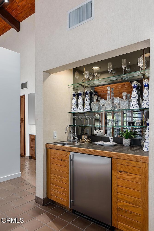 bar featuring visible vents, a sink, wet bar, dark tile patterned floors, and stainless steel refrigerator