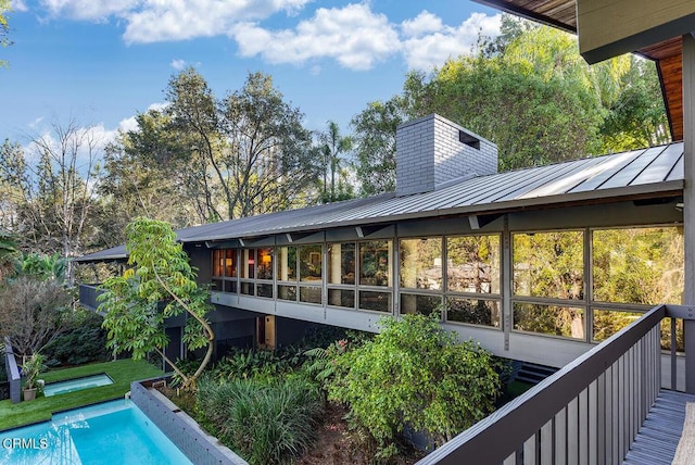 back of property with a standing seam roof, metal roof, an outdoor pool, and a sunroom