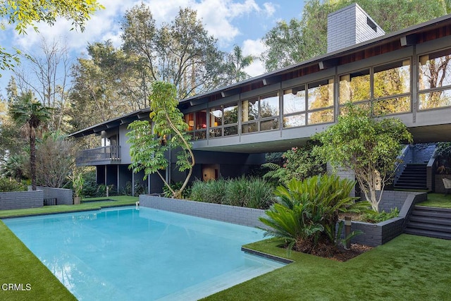 rear view of house featuring stairs, an outdoor pool, and a lawn