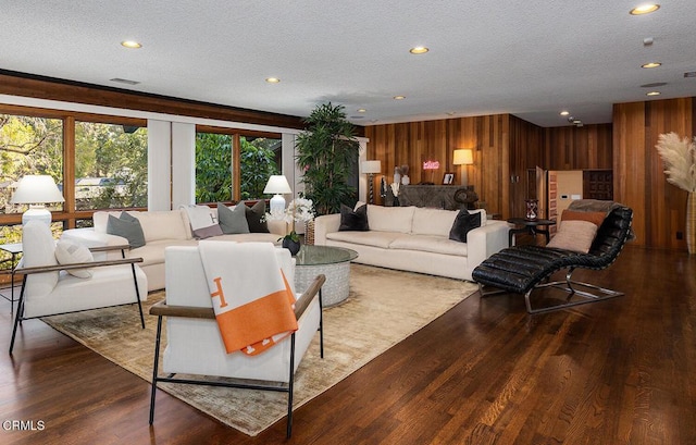 living room featuring a textured ceiling, dark wood-type flooring, recessed lighting, and wooden walls