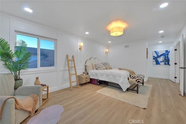 bedroom with light wood-type flooring, a decorative wall, and recessed lighting