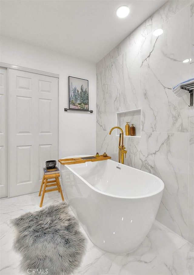 full bath featuring a freestanding tub, stone wall, and marble finish floor