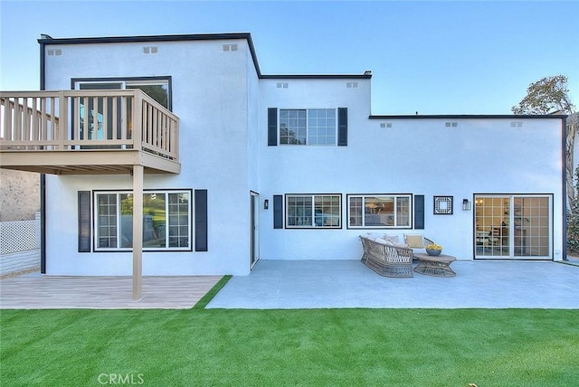 back of property with a balcony, a patio area, a lawn, and stucco siding