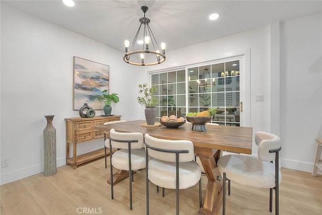 dining space with baseboards, light wood-style floors, and a notable chandelier