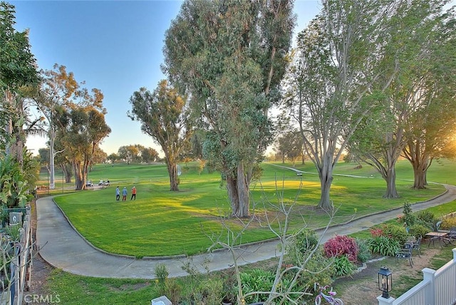 view of community featuring view of golf course, fence, and a yard