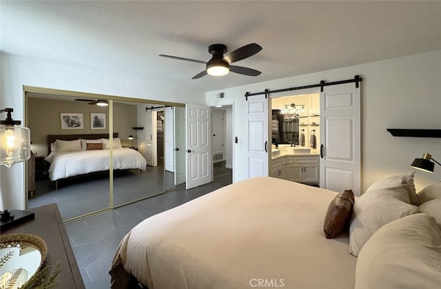 bedroom with a textured ceiling, a barn door, a ceiling fan, visible vents, and a closet