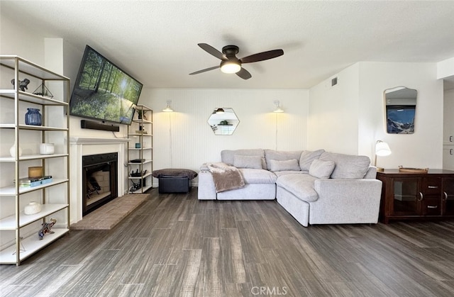 living area featuring visible vents, a fireplace with raised hearth, a ceiling fan, wood finished floors, and a textured ceiling