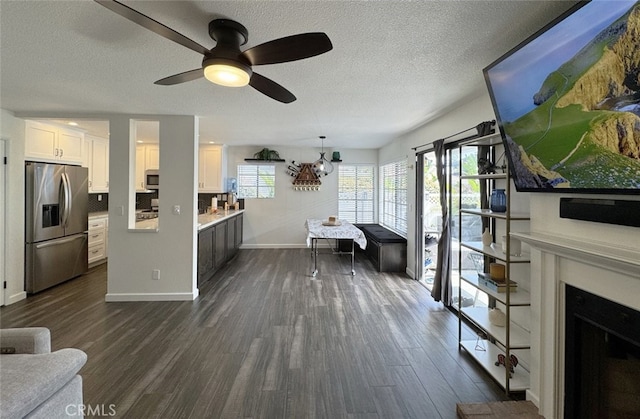 unfurnished living room featuring baseboards, dark wood finished floors, ceiling fan, a textured ceiling, and a fireplace