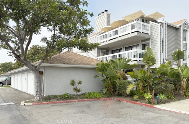 exterior space featuring stucco siding, roof with shingles, a chimney, and community garages