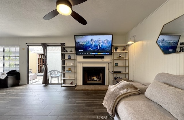 living room featuring a textured ceiling, a lit fireplace, ceiling fan, and wood finished floors