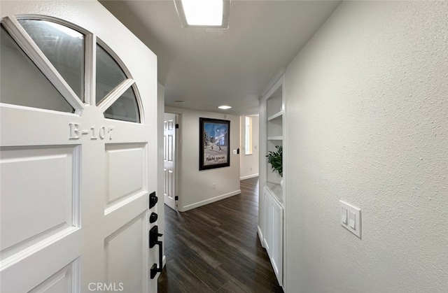 corridor with a textured wall, dark wood finished floors, and baseboards