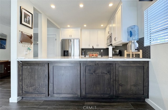 kitchen featuring a peninsula, appliances with stainless steel finishes, white cabinetry, and decorative backsplash