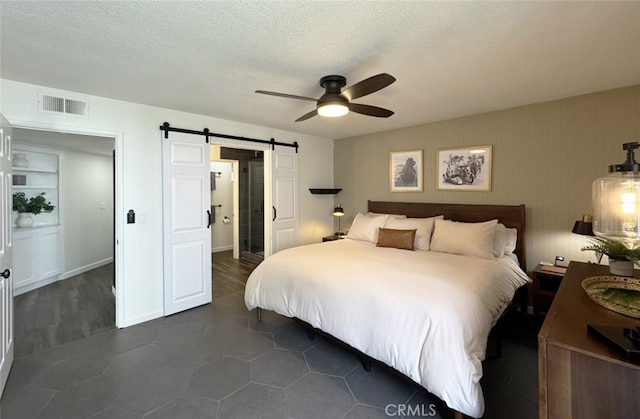 bedroom with a textured ceiling, a barn door, visible vents, and a ceiling fan