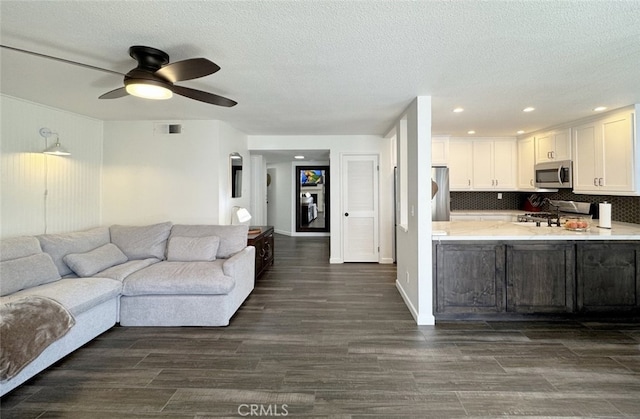 living area featuring dark wood finished floors, visible vents, a ceiling fan, a textured ceiling, and baseboards